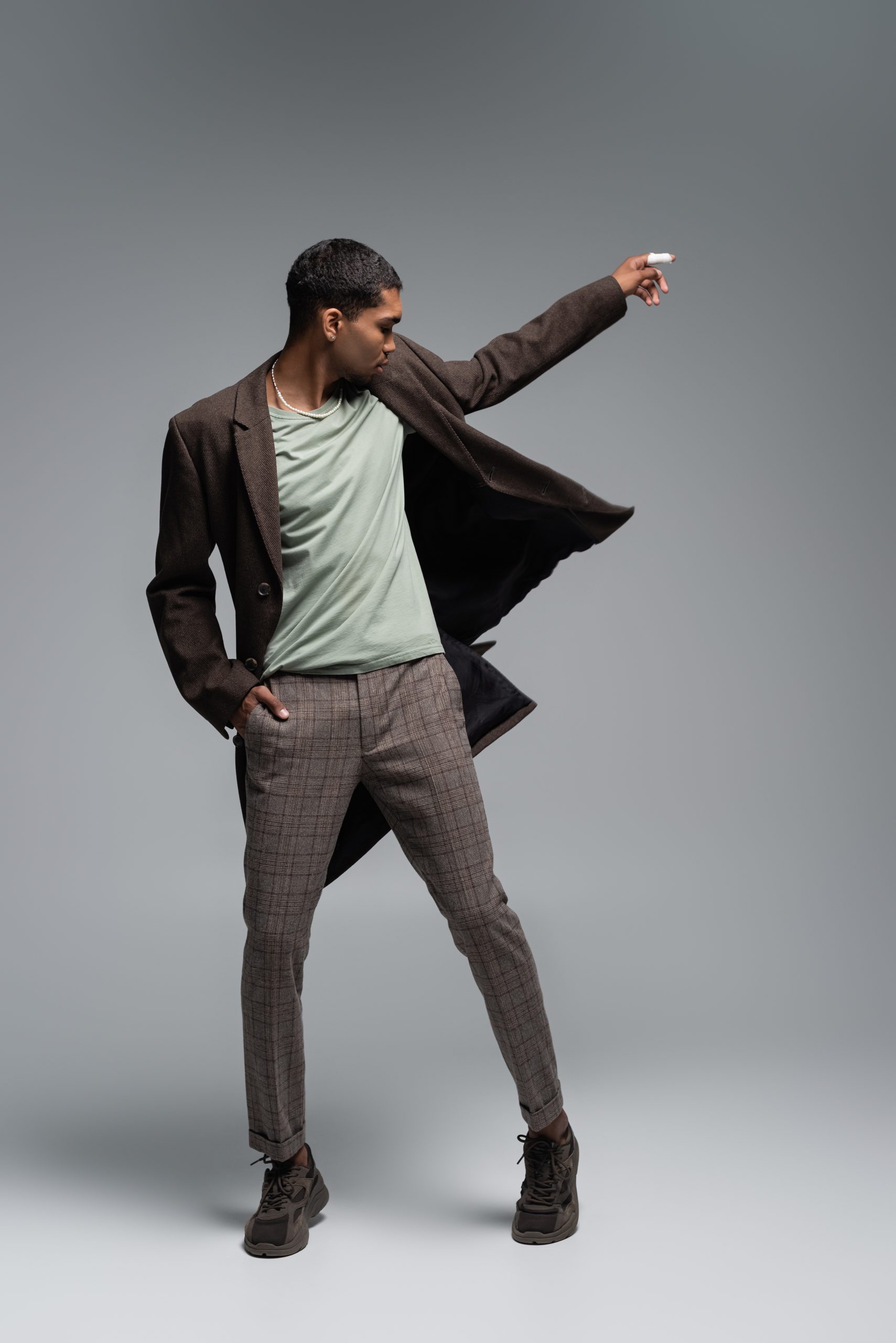 full length of young african american man in autumnal woolen coat posing with hand in pocket on grey